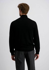 Schwarzer Strickpullover mit ribbeltem Kragen und Bündchen, kombiniert mit grauen, strukturierten Hosen. Der Fokus liegt auf Form und Material.