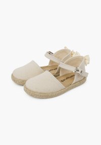 Beige canvas espadrilles met verstelbare band, jute afwerking en strikaccent bij de hiel. Vlakke, afgeronde teenontwerp.