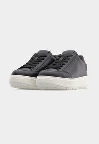 Ζευγάρι μαύρα δερμάτινα αθλητικά παπούτσια με λευκές σόλες, σχέδιο με κορδόνια και γλώσσα με λογότυπο, σε απλό ανοιχτό φόντο.