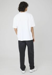 T-shirt en coton blanc à manches courtes, coupe décontractée et encolure arrondie, associé à un pantalon en denim foncé et des baskets blanches.