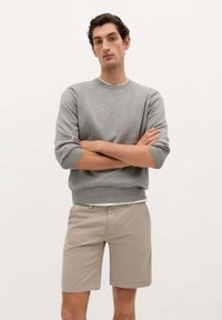Suéter de punto gris con cuello redondo y mangas enrolladas, combinado con pantalones cortos beige, que cuenta con un corte clásico y bolsillos delanteros.