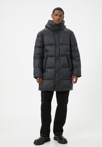 Sort puffjakke med hætte, med en quiltet design, frontlynlås og sidelommer. Båret med sorte bukser og kraftige støvler.