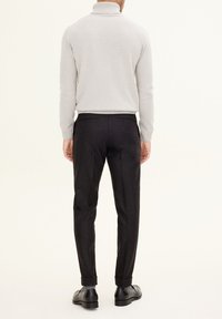 Light gray turtleneck sweater paired with dark slim-fit trousers. Smooth fabric with a ribbed collar, featuring tailored, detailed stitching.
