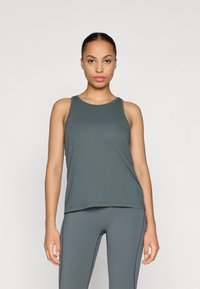 Tumši pelēkā krāsā sporta topiņš ar apaļu kakla izgriezumu, viegla auduma un brīvā piegriezuma, apvienots ar atbilstošām tumši pelēkām legingi.