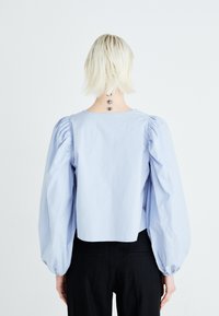 Gaiši zilas puff-sleeves tops ar apaļu kakla izgriezumu un salocītiem detaļām uz piedurknēm, apvienots ar melniem piegulošiem biksēm.