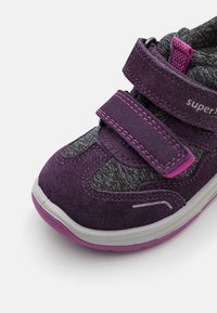 Fialová sportovní bota s semišovou a síťovinovou tkaninou, s páskem na suchý zip, růžovými akcenty a šedými podrážkami s bílými detaily.