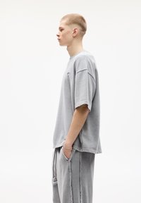Sivý oversized bavlnený tričko s poklesnutými ramenami a surovými okrajmi, kombinované s nenáročnými sivými nohavicami s voľným strihom. Minimalistický dizajn.