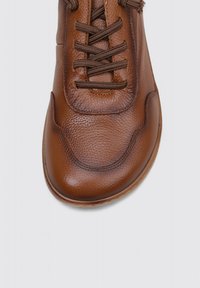 Zapatilla de cuero marrón con un acabado texturizado, puntera redonda y cordones marrones entrelazados. Presenta sutiles detalles de costura y una suela flexible.
