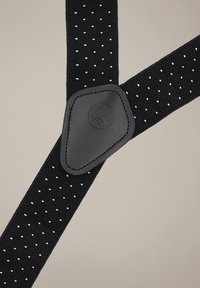 Czarne szelki wykonane z plecionego materiału, zdobione wzorami w kształcie diamentów i białymi kropkami, z czarnym skórzanym akcentem z logo.