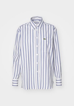 White button-up shirt with blue vertical stripes, a pocket, and a small green logo on the chest. Long sleeves with buttoned cuffs.