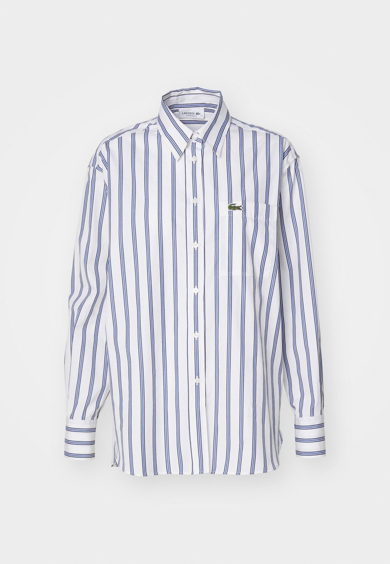 Camicia bianca con bottoni e strisce verticali blu, una tasca e un piccolo logo verde sul petto. Maniche lunghe con polsini abbottonati.