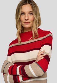 Roter und beiger gestreifter Pullover mit hohem Kragen, der eine gerippte Textur und unterschiedlich breite Streifen in den Farbtönen Rot, Beige und Creme aufweist.