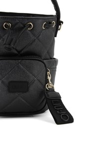 Borsa nera trapuntata con una texture liscia, occhielli dorati e una tracolla staccabile con logo impresso. Include una piccola tasca zip nella parte anteriore.