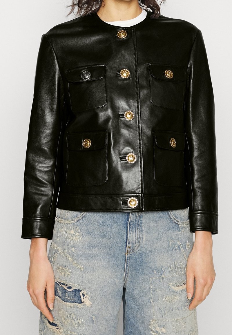 Černá kožená bunda s kulatým výstřihem, předními kapsami a zlatými dekorativními knoflíky. Hladká textura s dokonale padnoucím střihem.