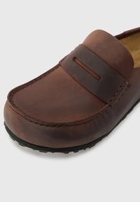 Barna bőrből készült, slip-on cipő, lekerekített orral, varrott díszítéssel és vízszintes pánttal ellátott, textúrált gumitalppal.