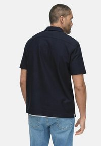 Donker marineblauw polo shirt met korte mouwen, een strak ontwerp, subtiele textuur en een rechte zoom, gedragen met lichtblauwe jeans.