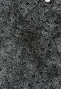 Un tissu en denim gris foncé avec de petits trous effilochés et une section de poche pliée, montrant une couture texturée et un bord de bouton argenté.