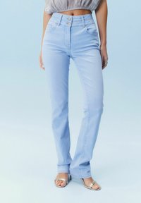 Jeans taille haute bleu clair avec deux poches avant et une fermeture à boutons. Le tissu a une texture lisse avec une légère extensibilité.