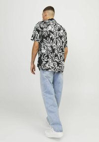 Camisa negra de manga corta con patrón floral blanco; jeans de mezclilla de corte relajado; modelo de espaldas, usando zapatillas blancas.