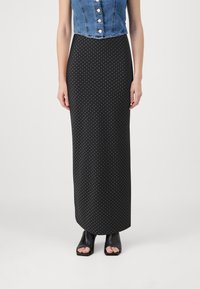 Top corto de mezclilla con botones y una falda maxi de lunares negros. La falda presenta un diseño ajustado y una textura suave. Zapatos negros de tacón abierto.