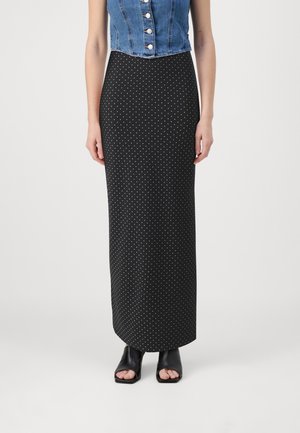 Haut en denim court avec des boutons et une jupe maxi à pois noirs. La jupe présente un design ajusté et une texture lisse. Chaussures noires à bout ouvert.