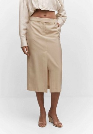 Falda beige hasta la rodilla con una abertura frontal, corte ajustado y textura suave. Combinada con una blusa de color claro y sandalias de cuña transparentes.
