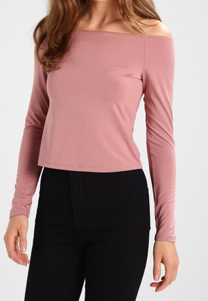 Schulterfreies, langärmeliges Oberteil aus weichem rosaroten Stoff. Hat ein kurzes Design und eine glatte Textur. Kombiniert mit schwarzen Hosen.