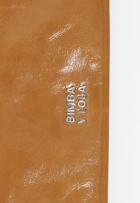 Beżowa sztuczna skórka o błyszczącej powierzchni; posiada wytłoczone na boku srebrne logo "BIMBA Y LOLA".