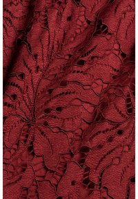 Rode textuurstof met een ingewikkeld bladenpatroon en uitsparingen, dat een gelaagd ontwerp vertoont en een licht verhoogd, geweven gevoel heeft.