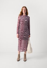 Lange mouw jurk van doorzichtig materiaal met een roze en zwarte geruite print, gecombineerd met beige enkellaarsjes en een witte handtas.