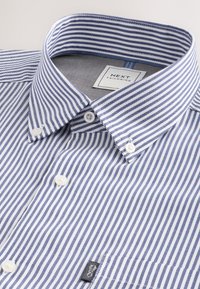 Chemise à rayures verticales bleues et blanches, boutonnée avec un col à boutons et une étiquette «Next Tailoring» à l'intérieur du col.