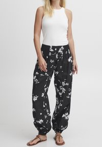 Svarta blommiga byxor med vita mönster, lös passform, smockad midja, uppvikta anklar. Bärs med en åtsittande vit linne och sandaler.