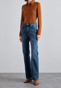 Rust-colored ribbed long-sleeve polo shirt paired with blue straight-leg jeans and brown pointed-toe heels, with a classic collar and button details.