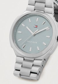 Silver stainless steel wristwatch with light blue dial, silver hour markers and hands, and a small red, white, and blue Tommy Hilfiger logo.