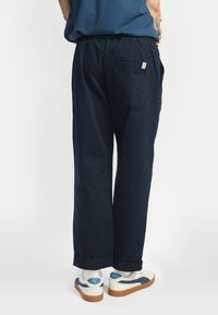 Pantaloni blu scuro realizzati in tessuto leggero, con vestibilità ampia, tasche laterali e orlo arrotolato, abbinati a sneakers bianche e blu.