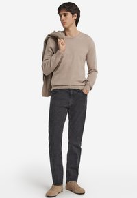 Beige stickad tröja med rund halslinning, mörkgrå denimjeans och ljusbruna sneakers. Tröjan hänger löst över axlarna, avslappnad passform.