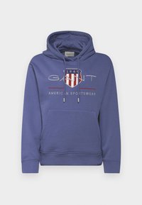 Felpa con cappuccio blu in misto cotone, dotata di tasca frontale. Presenta un logo a scudo stampato con testo in rosso e bianco.