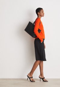 Musta olkalaukku, oranssi istuva neule, musta polvimittainen hame ja mustat korkokengät. Yksinkertainen muotoilu, sileät pinnat, moderni siluetti.