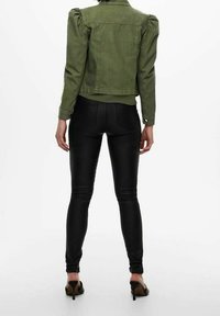 Olivengrønt denimjakke med puffede ærmer, parret med sorte læderleggings og sorte hælede sandaler, set fra ryggen.