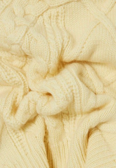 Tela de punto color crema suave con patrones de cables y acanalados, mostrada en primer plano con pliegues y detalles de textura.