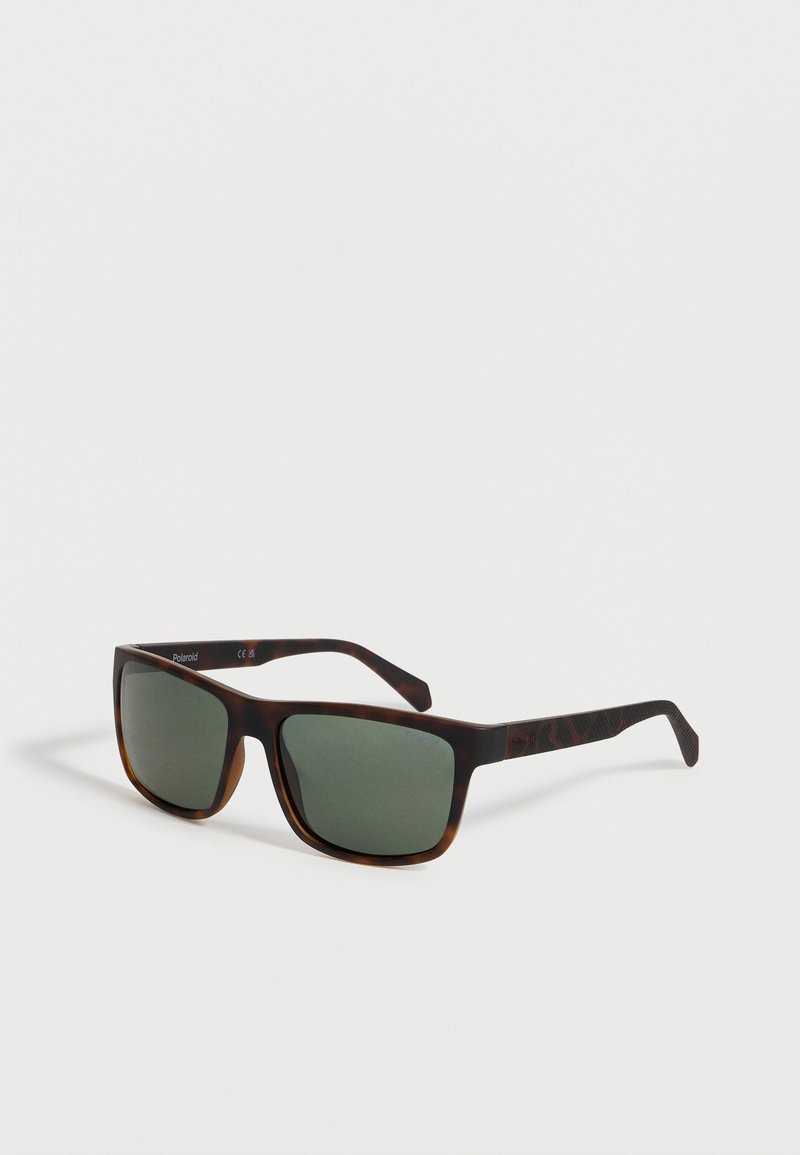 Ορθογώνια γυαλιά ηλίου με σκελετό από χελώνα και σκούρους πράσινους φακούς που τοποθετούνται σε λευκή επιφάνεια με κλίση προς τα δεξιά.