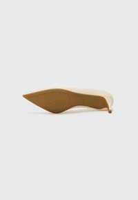 Chaussure à talon haut beige vue de la semelle, présentant un bout pointu et une semelle extérieure marron clair texturée pour une meilleure adhérence.