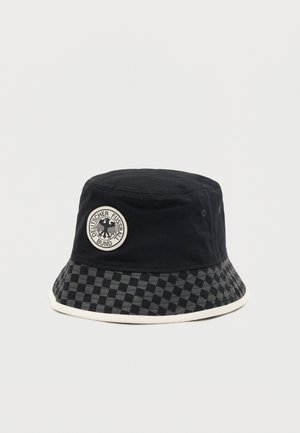 Μαύρο καπέλο τύπου κουβά με καρό γείσο και κυκλικό μπάλωμα που απεικονίζει το λογότυπο αετού της Γερμανικής Ποδοσφαιρικής Ομοσπονδίας.