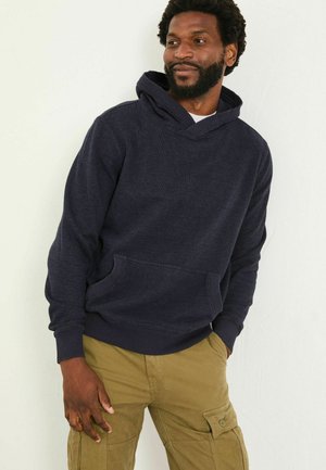 Navy hoodie with a textured design, drawstring hood, and front pocket. Paired with light khaki cargo pants, featuring side pockets.