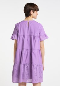 Lilla bomuldskjole med korte volangærmer, tiered design og broderi anglaise-detaljer ved kanten, med en nøglehulslukning i ryggen.