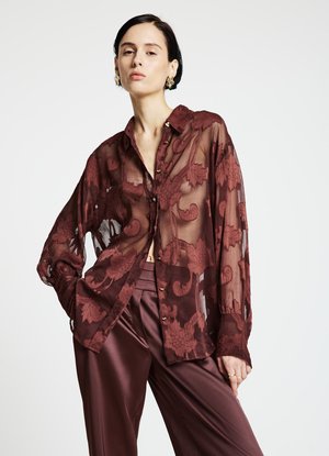 Chemise transparente bordeaux avec broderie florale, manches longues, fermeture à boutons et coupe décontractée, associée à un pantalon en satin bordeaux.