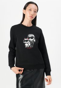 Felpa nera in misto cotone, con una grafica in stile cartoon di una figura e un gatto con occhiali da sole, con dettagli rossi e polsini a coste.