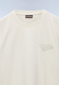 Cremefarvet kortærmet t-shirt lavet af bomuld. Har en rund halsudskæring og et mat logo trykt på venstre brystområde.