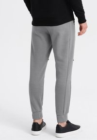 Graue Jogginghosen mit tapered Fit, elastischen Bündchen, Seitentaschen und strukturierten Seiteneinsätzen. Getragen mit schwarzen Sneakers.