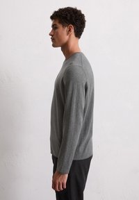 Graues Langarmshirt mit Rundhalsausschnitt, glatter Textur und figurbetontem Design, kombiniert mit schwarzen Hosen, von der Seite gezeigt.